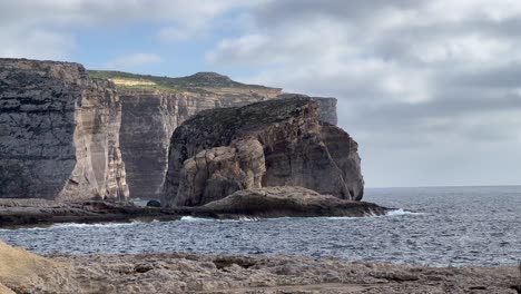 Toma-En-Mano-De-4k-Que-Captura-La-Belleza-Rústica-De-La-Costa-De-La-Bahía-De-Dwejra,-Isla-De-Gozo,-Malta:-Olas-Del-Mar-Mediterráneo-Rompiendo-Contra-Formaciones-Rocosas-Icónicas-En-Un-Entorno-Pintoresco