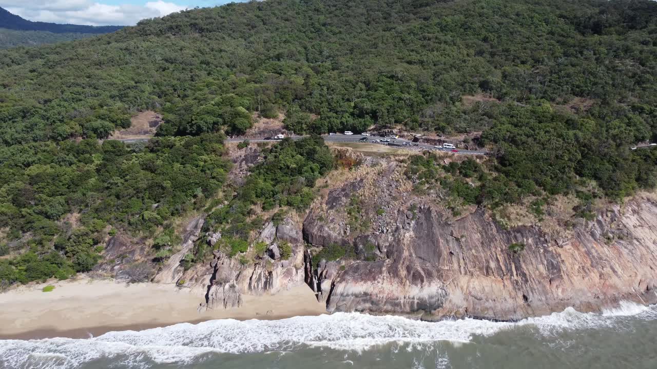 4K Aerial view of rocky cliff and a small sandy beach with a coastal highway in the background