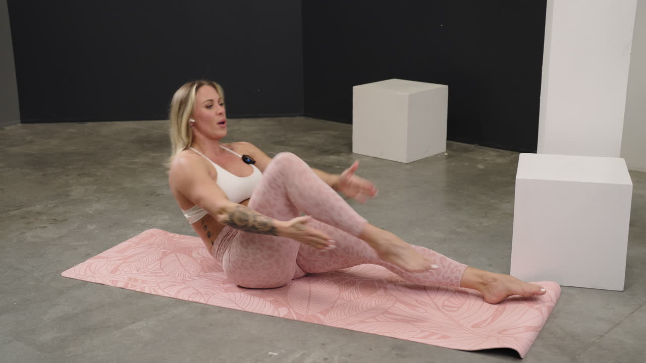 Fitness woman practicing an engaging core strengthening exercise in a studio space, leaning back and exploding to touch toes with hands