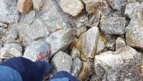 punto de vista hasta los zapatos del caminante pisando piedras para cruzar un arroyo alpino