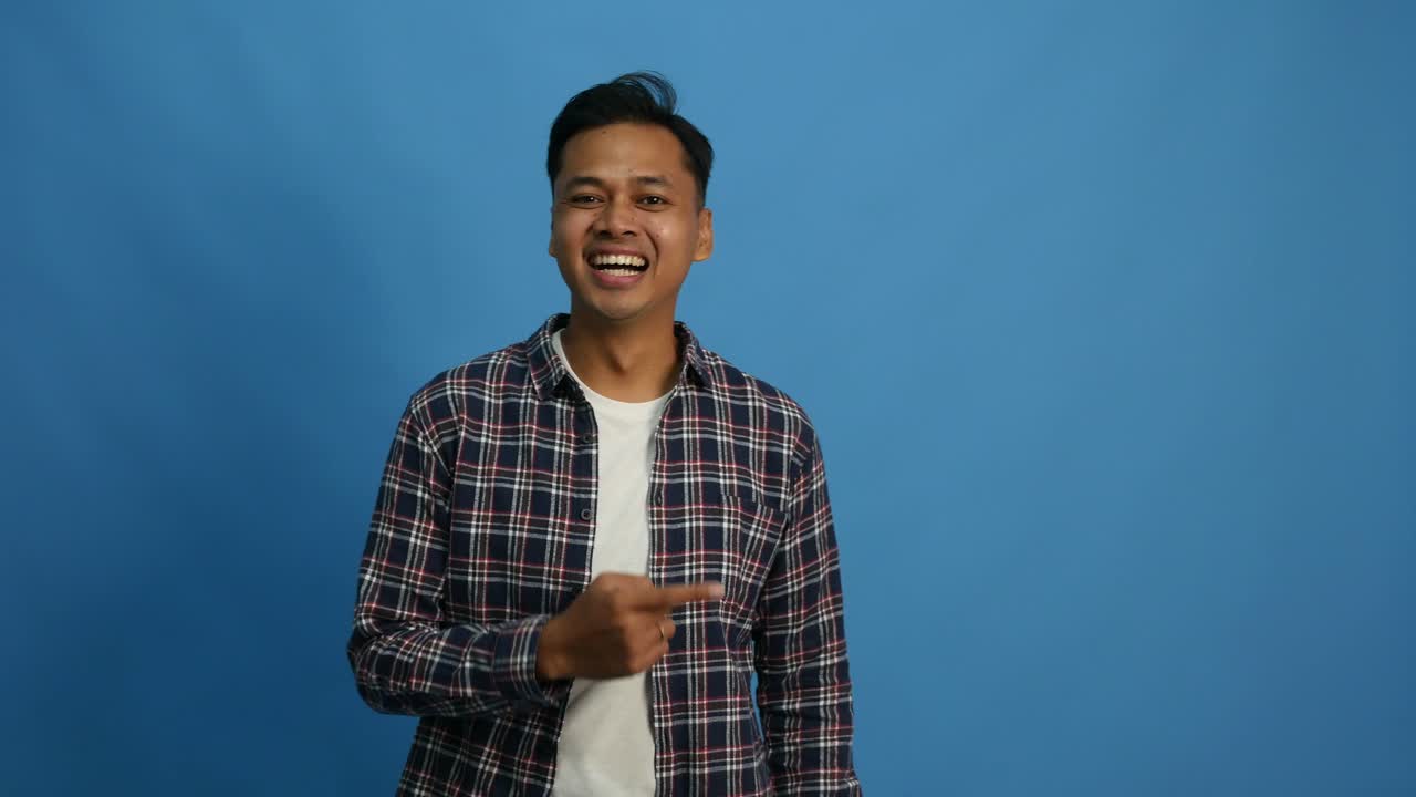 Recommending Asian man pointing at right side, copy space. Male presenting, showing something isolated on blue background