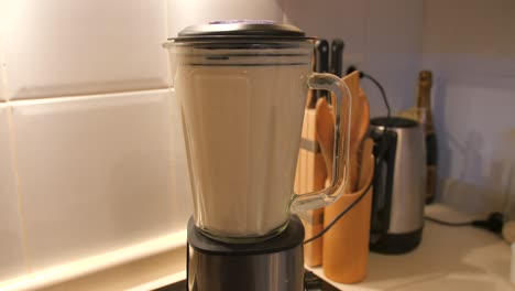 view of homemade oat and milk mix grinding in a blender making oat milk in the kitchen with white tile in the background