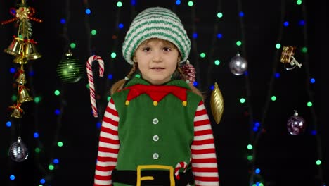 teen kid girl in christmas elf santa claus helper costume showing thumbs up on black background