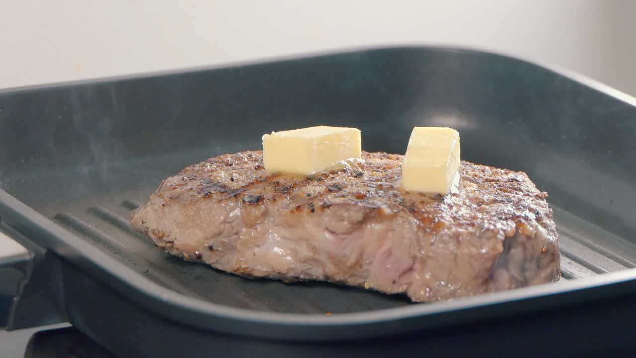Slow Motion Shot of Adding Butter to a Ribeye Steak in a Hot Pan