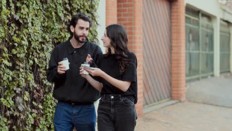 Couple walking and talking outdoors while holding coffee and looking at a phone