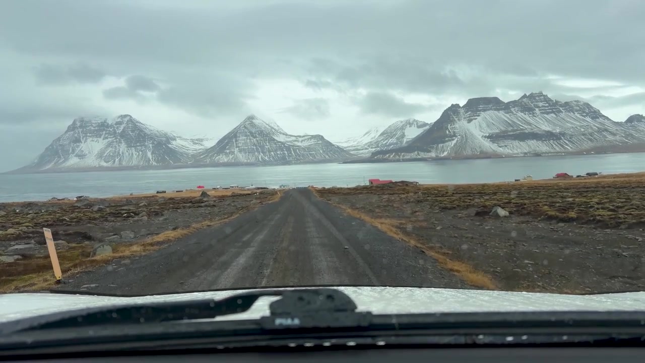 Auto che guida su una strada sterrata che porta verso il fiordo con montagne innevate a Gjogur, Islanda. - Ripresa POV