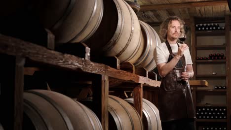 authentic shot of successful male sommelier is tasting a flavor and checking white wine quality poured in transparent glass in a wine cellar.