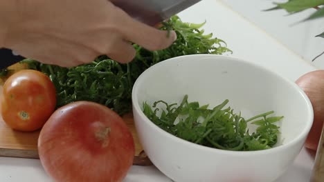 Cutting-the-tender-shoots-of-fiddlehead-with-a-knife-and-placing-it-in-a-bowl-to-make-pako-salad,-a-local-Filipino-delicacy-showing-the-authentic-daily-home-life-and-culinary