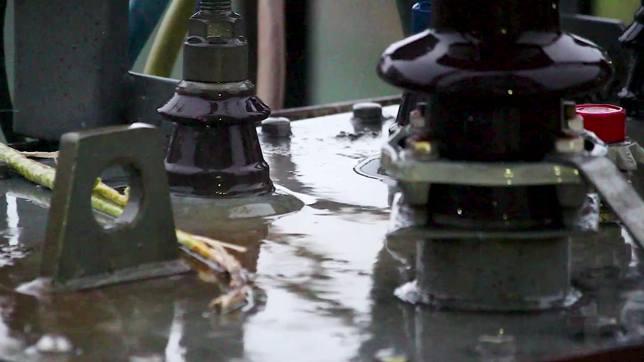 Electrical insulators and power equipment covered with rainwater at substation, showing wet industrial infrastructure for energy, engineering, electricity and weather projects.