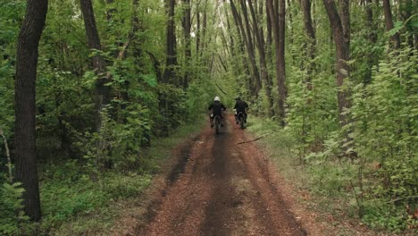 back view of two motocross riders riding on a dirt road in the forest