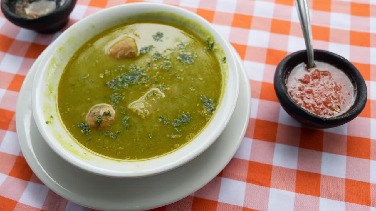 Herkullinen ja täyttävä kolumbialainen sancocho de gallina lähikuvassa ruudullisella pöytäliinalla. Eloisaa keittoa täydentää mausteinen salsa, luoden värikkään näkymän.