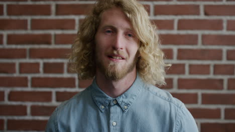 portrait happy young blonde man student turns head laughing enjoying successful lifestyle cheerful bearded hipster guy looking at camera brick wall background