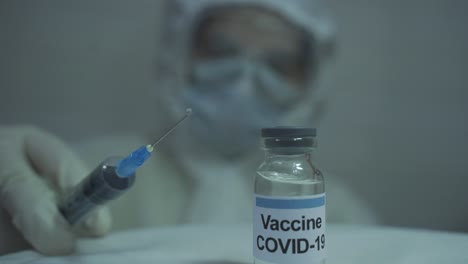 human wearing protective ppe kit carefully spilling out medicine from a syringe filled with covid 19 vaccine