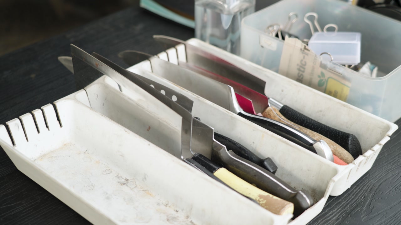Close-up of assorted kitchen knives in a tray inside a knife sharpening workshop in Malaysia, showing professional tools, blade preparation, maintenance process, and organized workspace in UHD detail.