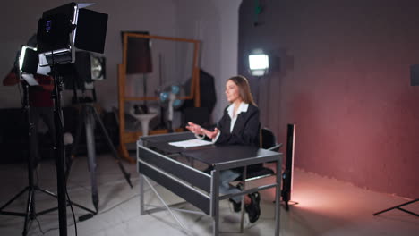 soffits are set to light the woman sitting at desk. brunette female reporter talks to camera gesturing.