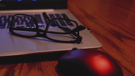 RIGHT-TO-LEFT-PAN-SHOT-OF-A-COMPUTER-SITTING-AT-A-KITCHEN-TABLE-WITH-GLASSES-LAYING-NEXT-TO-THE-KEYBOARD-AND-A-MOUSE-IN-THE-FOREGROUND