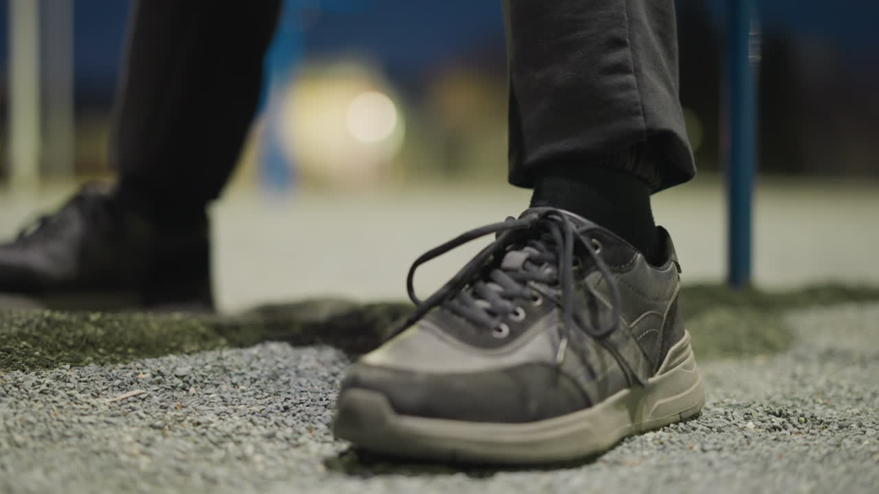 다리 사이에 축구공을 들고 벤치에 앉아있는 남자의 클로즈업, 그는 흐릿한 배경으로 반복적으로 땅에 발을 고 있습니다.