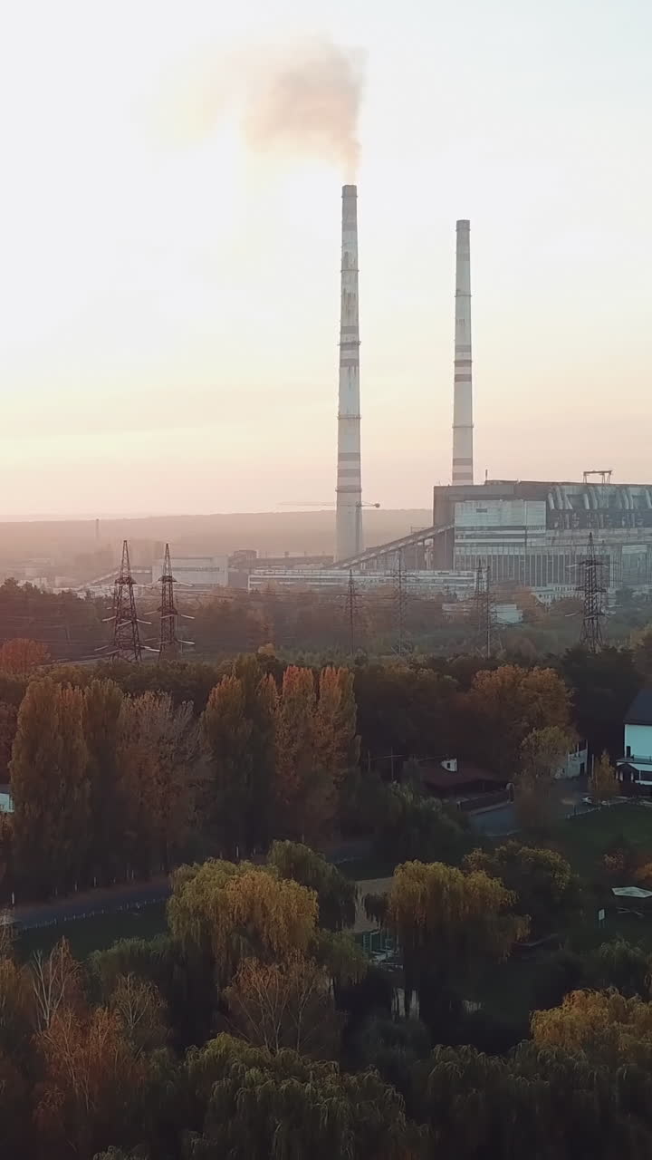 power plant with two pipes is located on the outskirts of the city on the bank of river. Camera motion back. Aerial view Vertical video