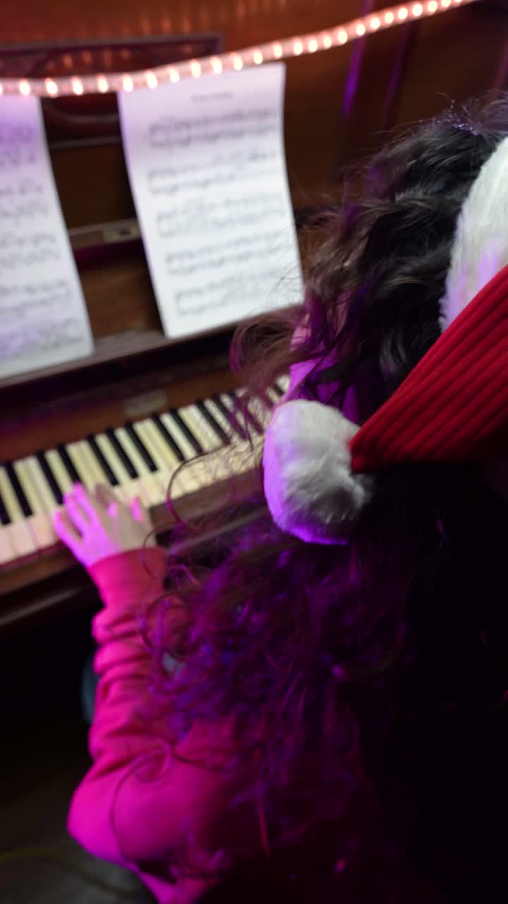 Young woman wearing a Santa hat plays Christmas music on a piano with festive lights and sheet music. Capture the joy and warmth of holiday traditions and musical expressions.