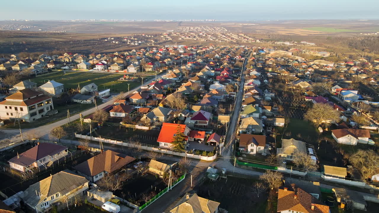 Aerial drone view of a village. View of multiple residential buildings, country roads, bare trees and football field. City on the background. Sunny weather. Moldova