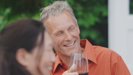 Group-Of-Mature-Friends-Talking-And-Drinking-Wine-At-Summer-Drinks-Party-In-Garden-At-Home