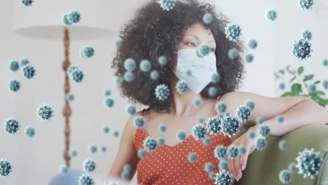 animación de células de coronavirus sobre una mujer afroamericana que usa una máscara facial en casa