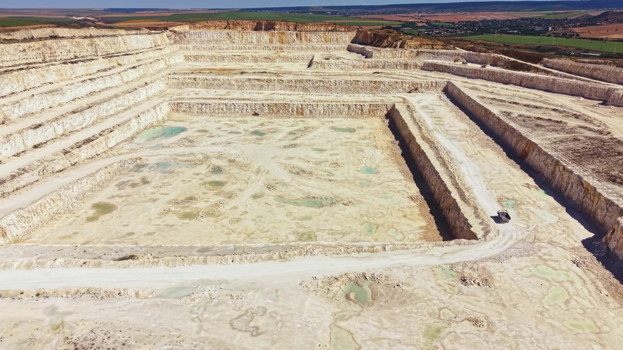 Quarry located in an open area with layers of earth and water pools visible at different levels during the day