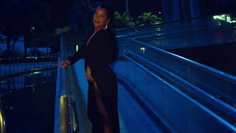 sexy hispanic woman spins in the walkway of a glass building wearing a black dress at night