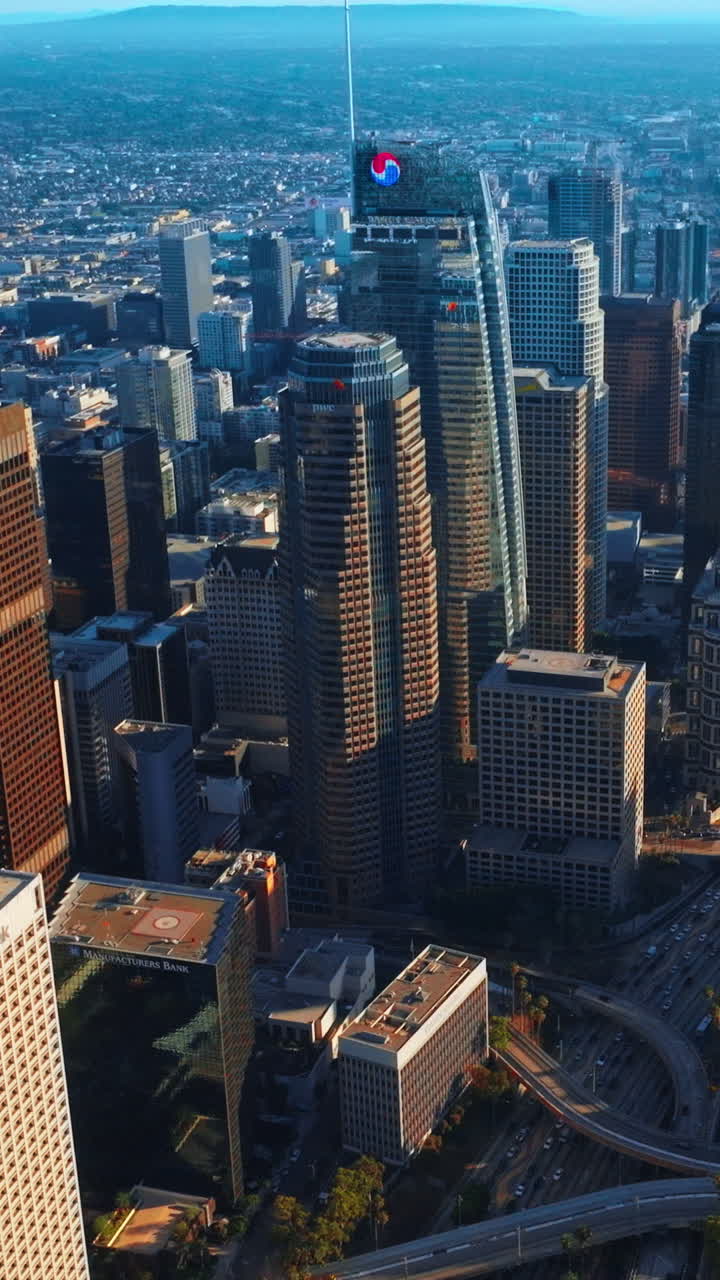 Flying over the stunning skyscrapers in downtown Los Angeles. Multi-lane highway with hundreds of cars passing through the city centre. Aerial view. Vertical video