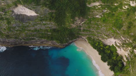 secluded tropical beach with tall cliffs on nusa penida island, aerial