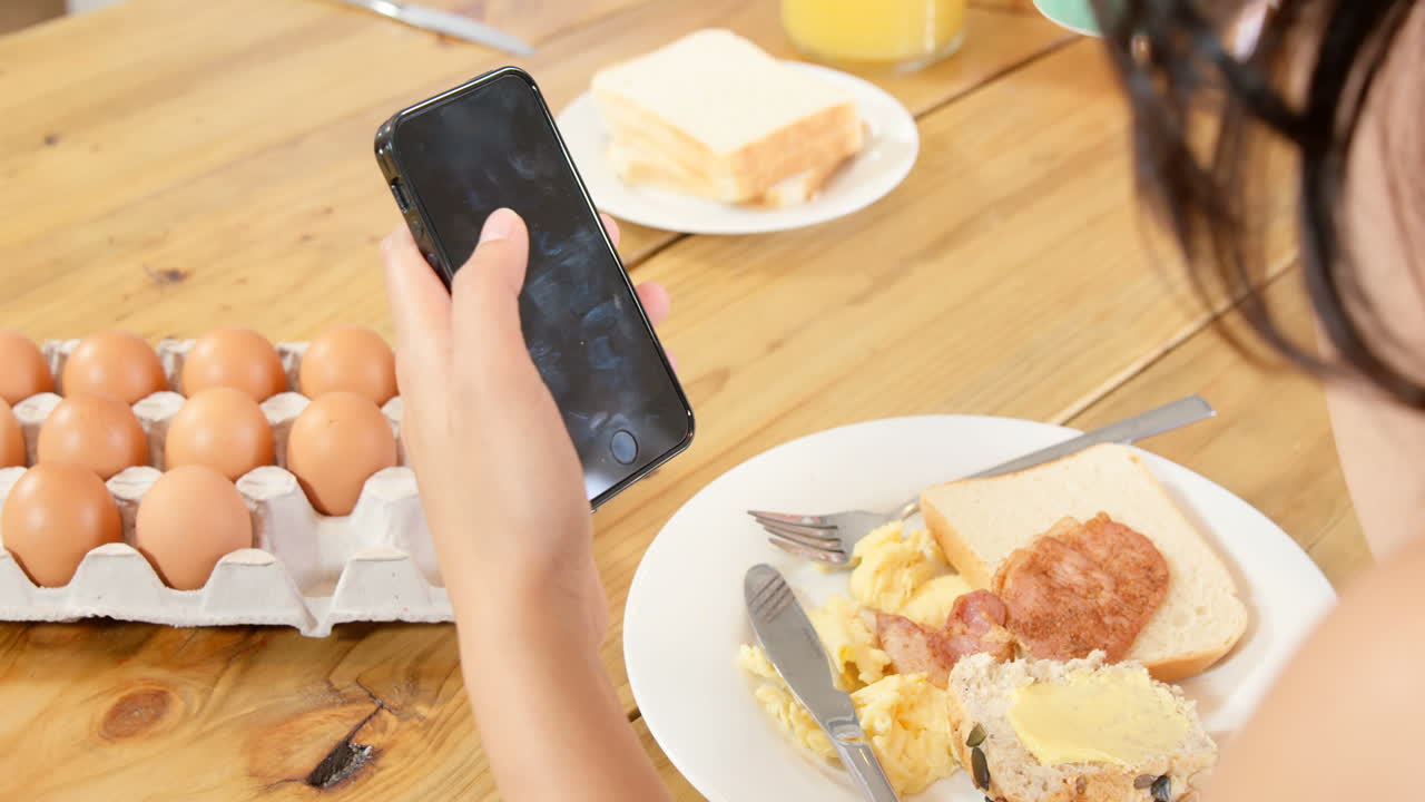 mujer usando su teléfono inteligente mientras desayuna