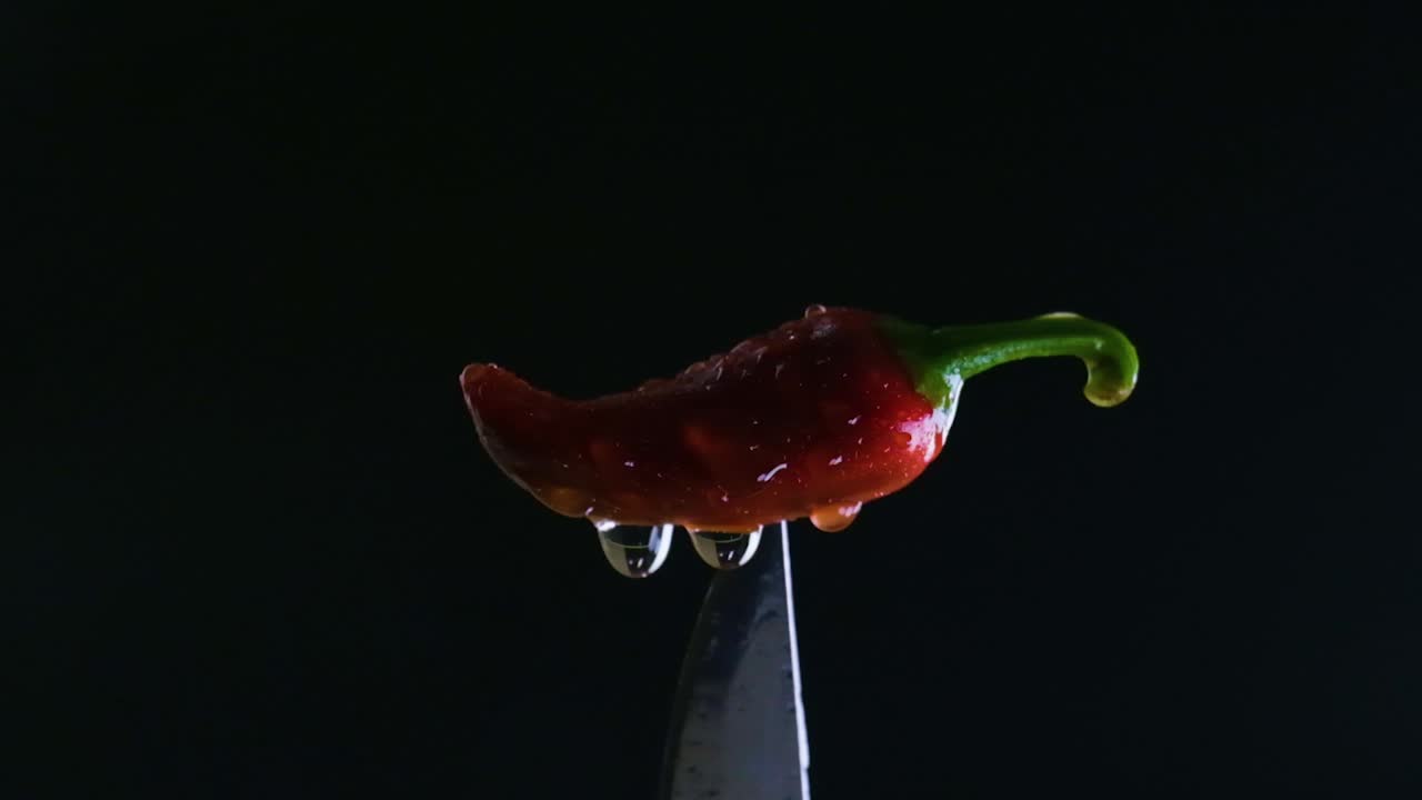 Spicy chili's brilliance, changing light and water drops on red jalapeno above knife