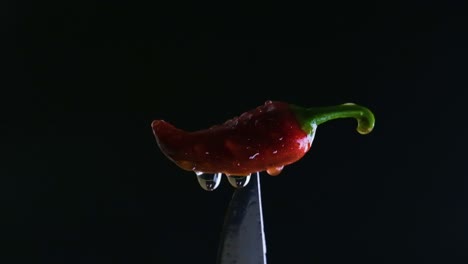 Spicy-chili's-brilliance,-changing-light-and-water-drops-on-red-jalapeno-above-knife