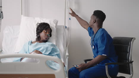 african-american woman resting in hospital bed after surgery talking to young male nurse. portrait of african-american nurse assisting ill female patient lying in bed