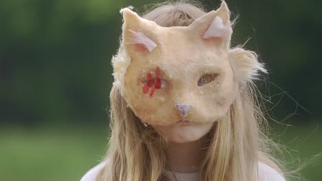 portrait of a girl in a cat mask standing in the middle of greenery