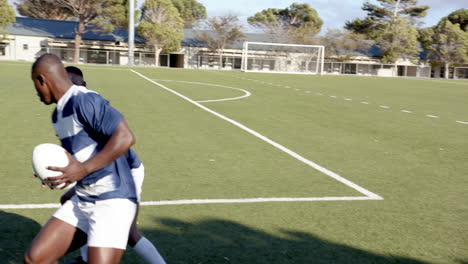 playing rugby, two african american men in sports uniforms passing ball on field