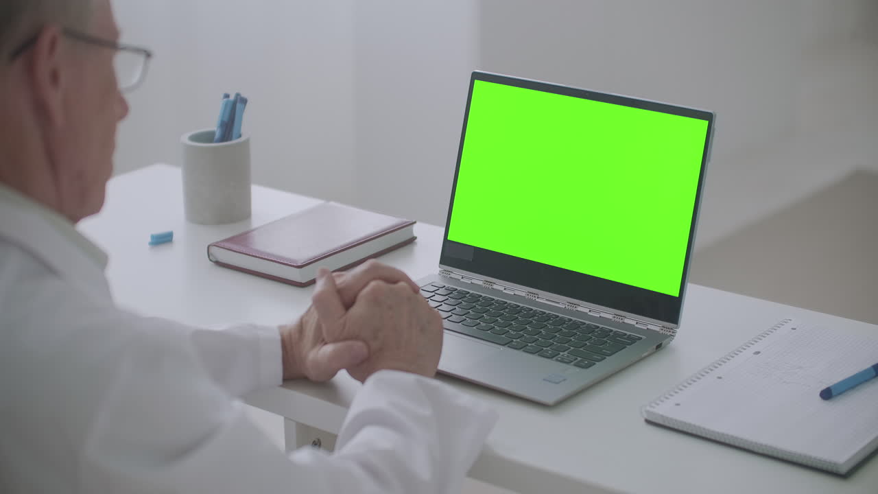 el médico está mirando la pantalla verde del portátil comunicando el concepto de llamada de video en línea