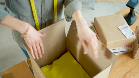 Vista-Superior-De-Las-Manos-Femeninas-Envolviendo-El-Paquete,-Poniendo-Ropa-En-La-Caja-Y-Cerrando-La-Caja-Con-Cinta-Adhesiva-Mientras-Prepara-El-Pedido-Para-El-Envío