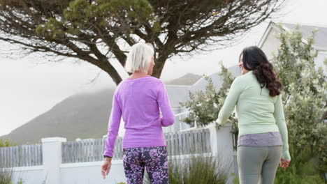 two diverse senior women walking on path and talking on sunny day, slow motion