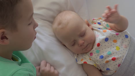 boy lying on a bed with his baby sister and stroking on her head