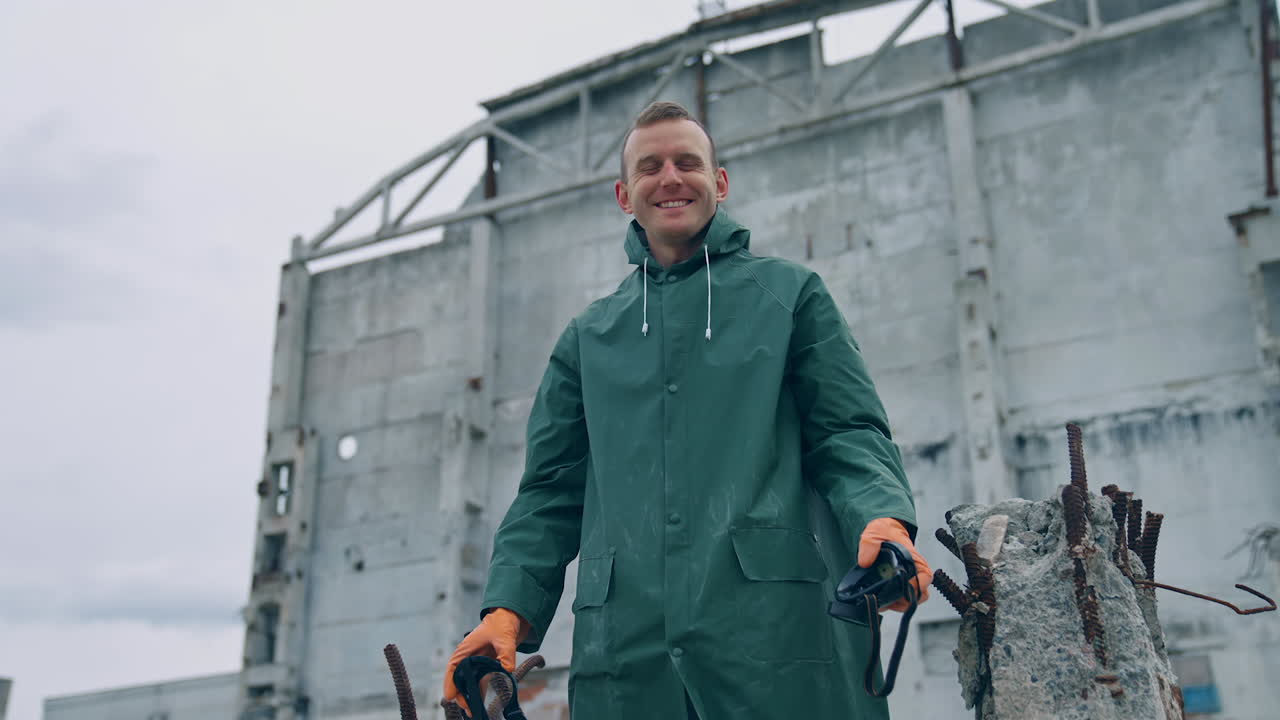 Happy ecologist in abandoned place. Man survivor holding gas mask in hands and smiles breathing fresh air on the background of destroyed building.