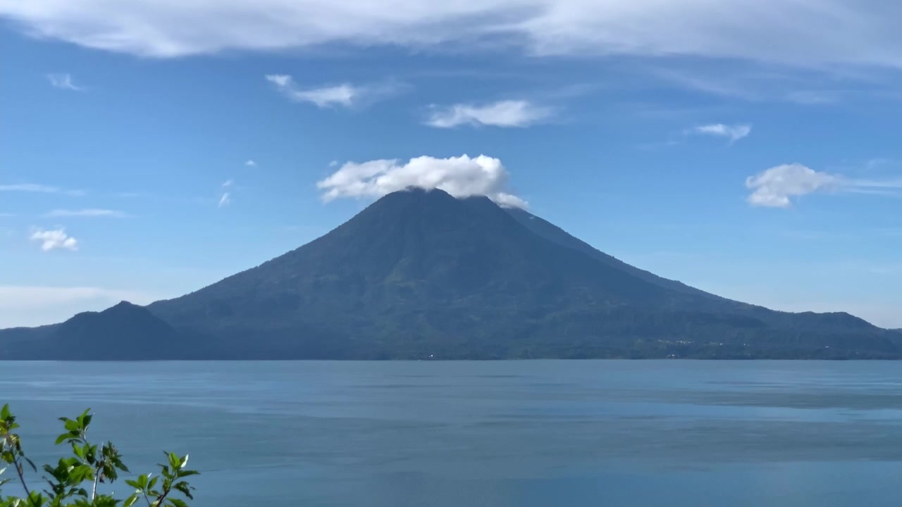 Timelapse af vulkanen Volcan de Atitlan i Atitlán-søen, Guatemala, Centralamerika, på en blå solskinsdag med skyer, der ruller over bjergtoppen, og brisen, der blæser over det blå søvand