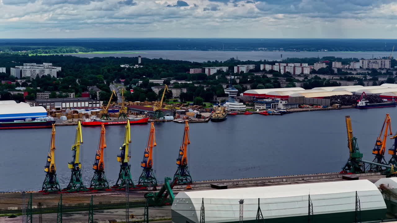 Bustling Freeport of Riga, Latvia, with its massive cargo cranes, docked ships, and industrial terminals lining the Daugava River - Aerial Parallax
