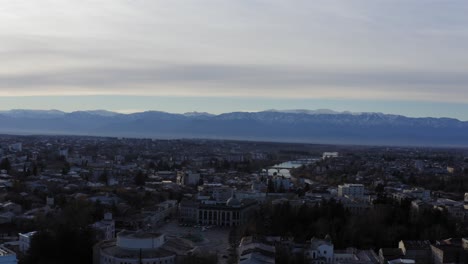 Vuelo-Aéreo-Sobre-La-Ciudad-De-Kutaisi-Con-Montañas-Nevadas-Y-El-País-Del-Río-Georgia