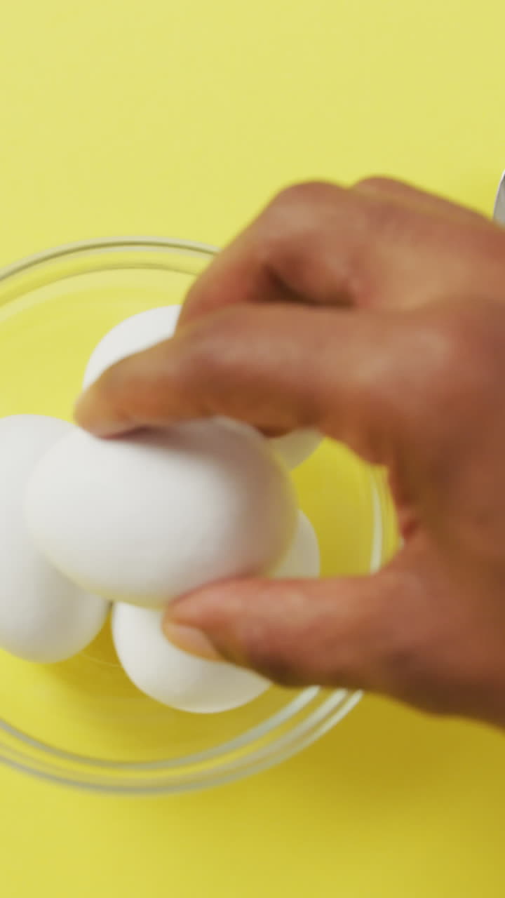 Video of close up of biracial man putting egg into bowl on yellow background