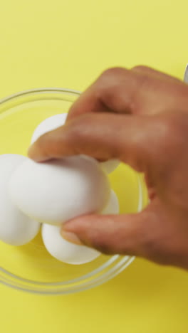 video of close up of biracial man putting egg into bowl on yellow background