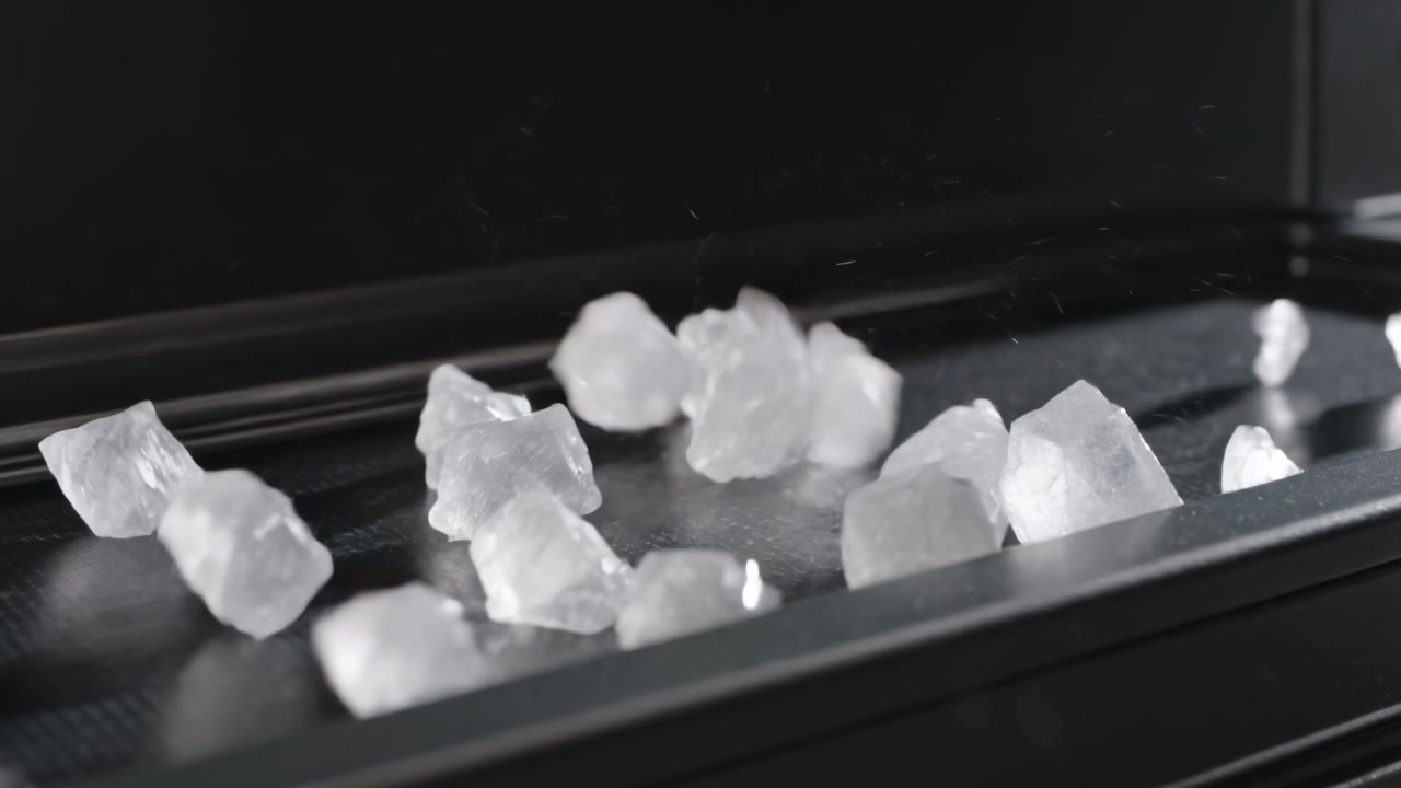 Crystals dropping offscreen, bouncing, scattering across dark tray, piling, glinting for food