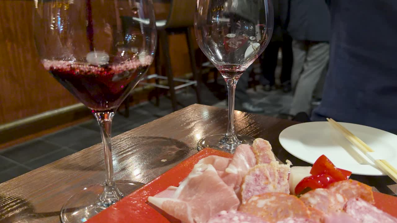 Vino rosso che si versa in un calice accanto a un piatto di carne sotto l'illuminazione calda di un ristorante