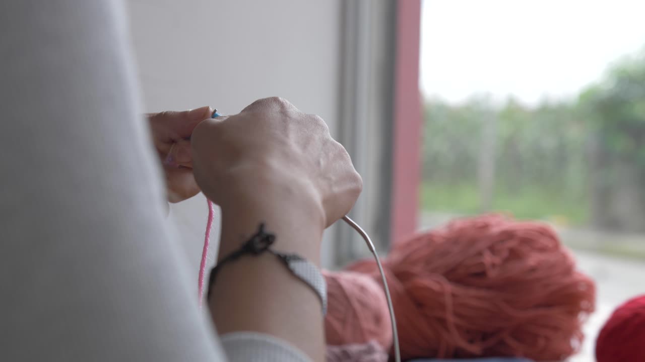 женщина петли и крюки пряжи во время вязания глядя в окно у реки