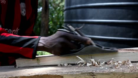 Carpenter-in-Nairobi,-Kenya-using-a-hand-plane-to-shape-and-smooth-a-piece-of-wood-for-a-furniture-project